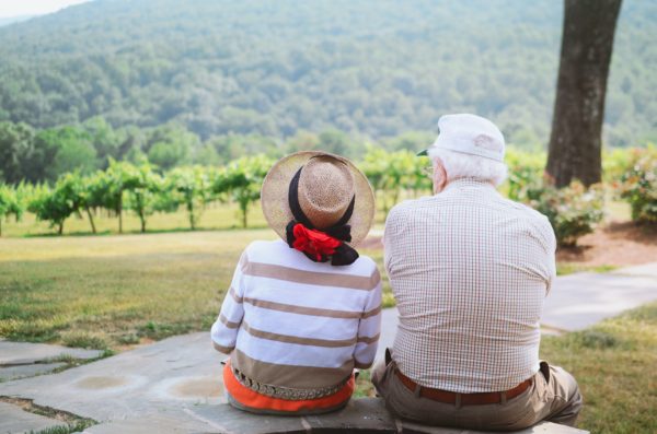 Elderly couple sitting on a stone wall looking out.