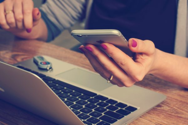 Woman using computer and holding cell phone