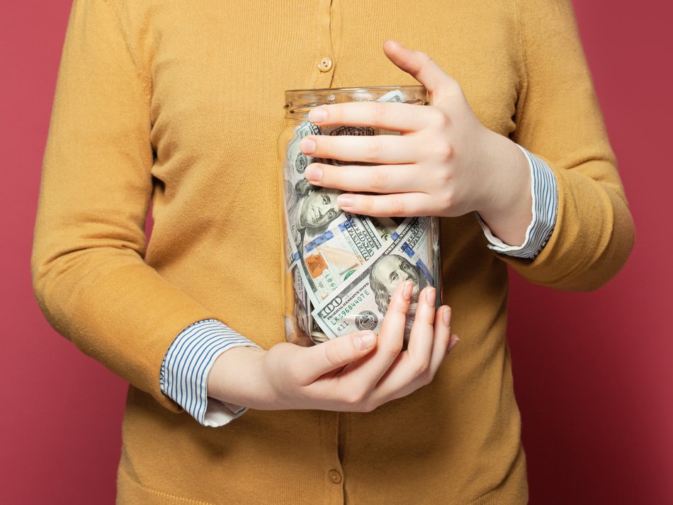Woman in yellow sweater holding jar of money