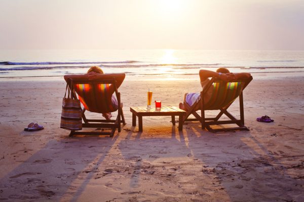 Couple sitting on the beach in lawn chairs watching the sunset.