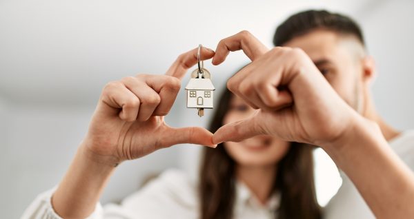 Young hispanic couple doing heart symbol with fingers and holding key of new home.