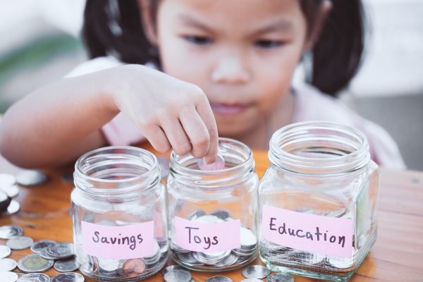 Young Asian girl placing coins in glass jars