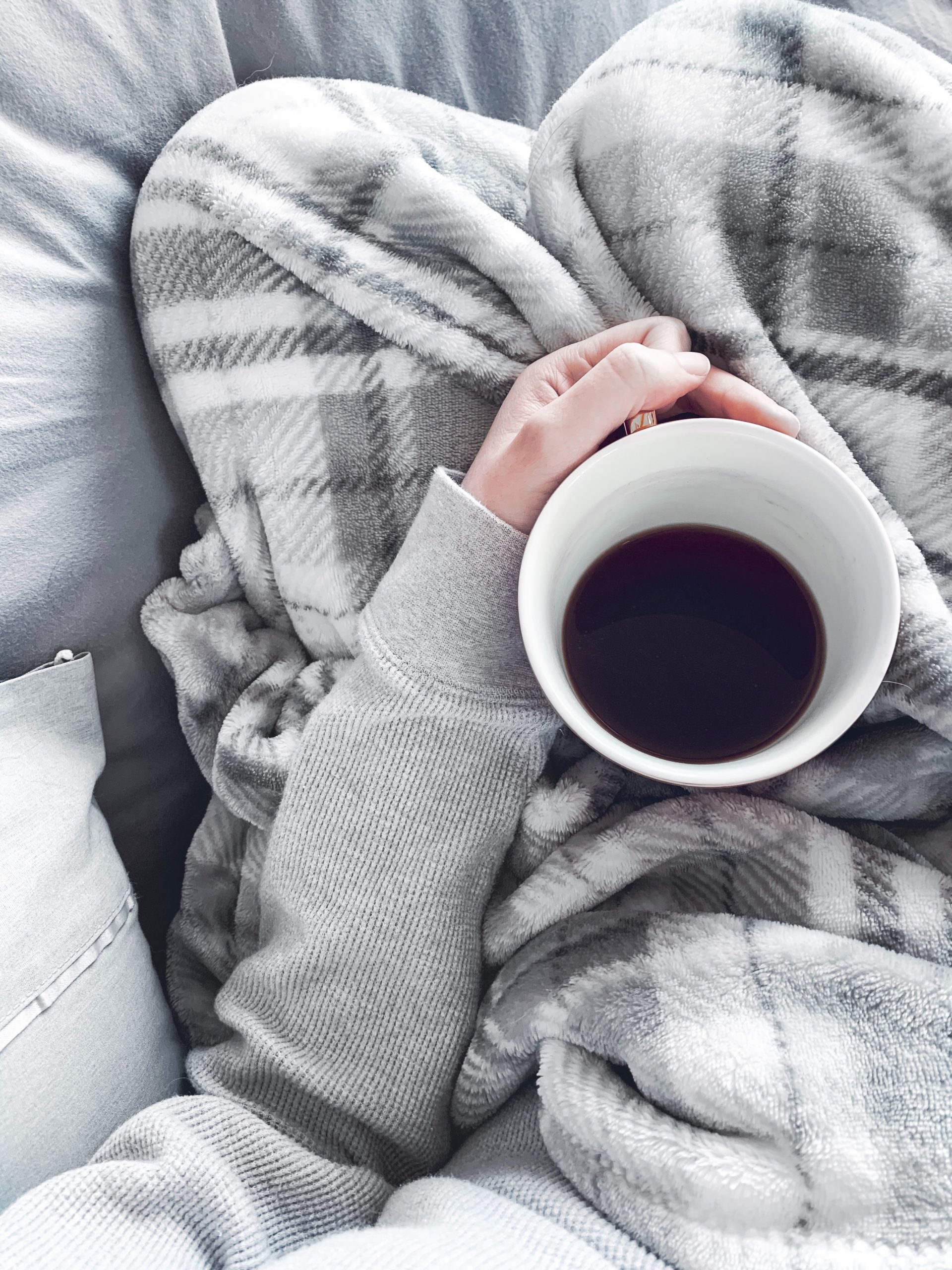 Photo of a woman sitting with a blanket and cup of coffee.